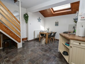A compact kitchen with a dining area, wooden staircase, and a skylight. - Saddlers Cottage (Weymouth)