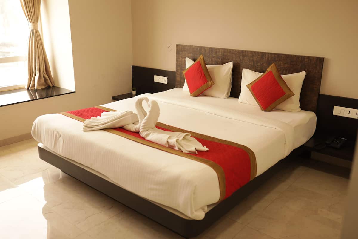 Uma cama bem arrumada com colcha vermelha e branca, uma almofada combinando em vermelho e branco e uma toalha branca sobre a cama.