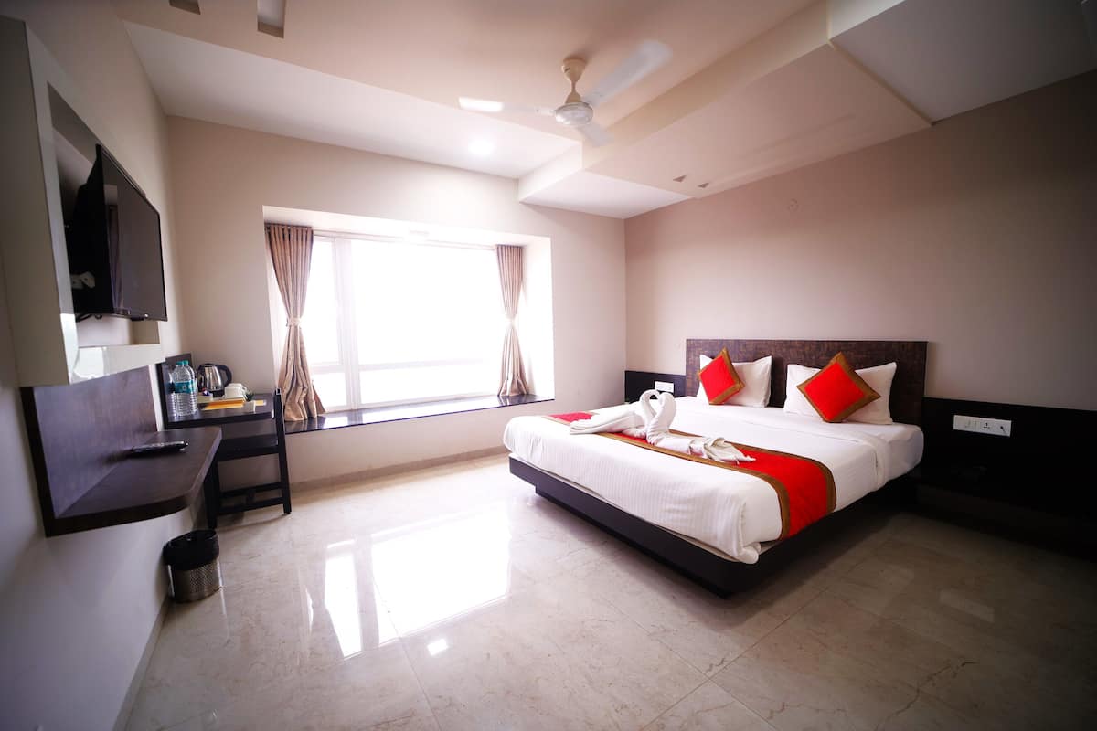 Quarto de hotel com cama, escrivaninha, cadeira, televisão e janela com cortinas.