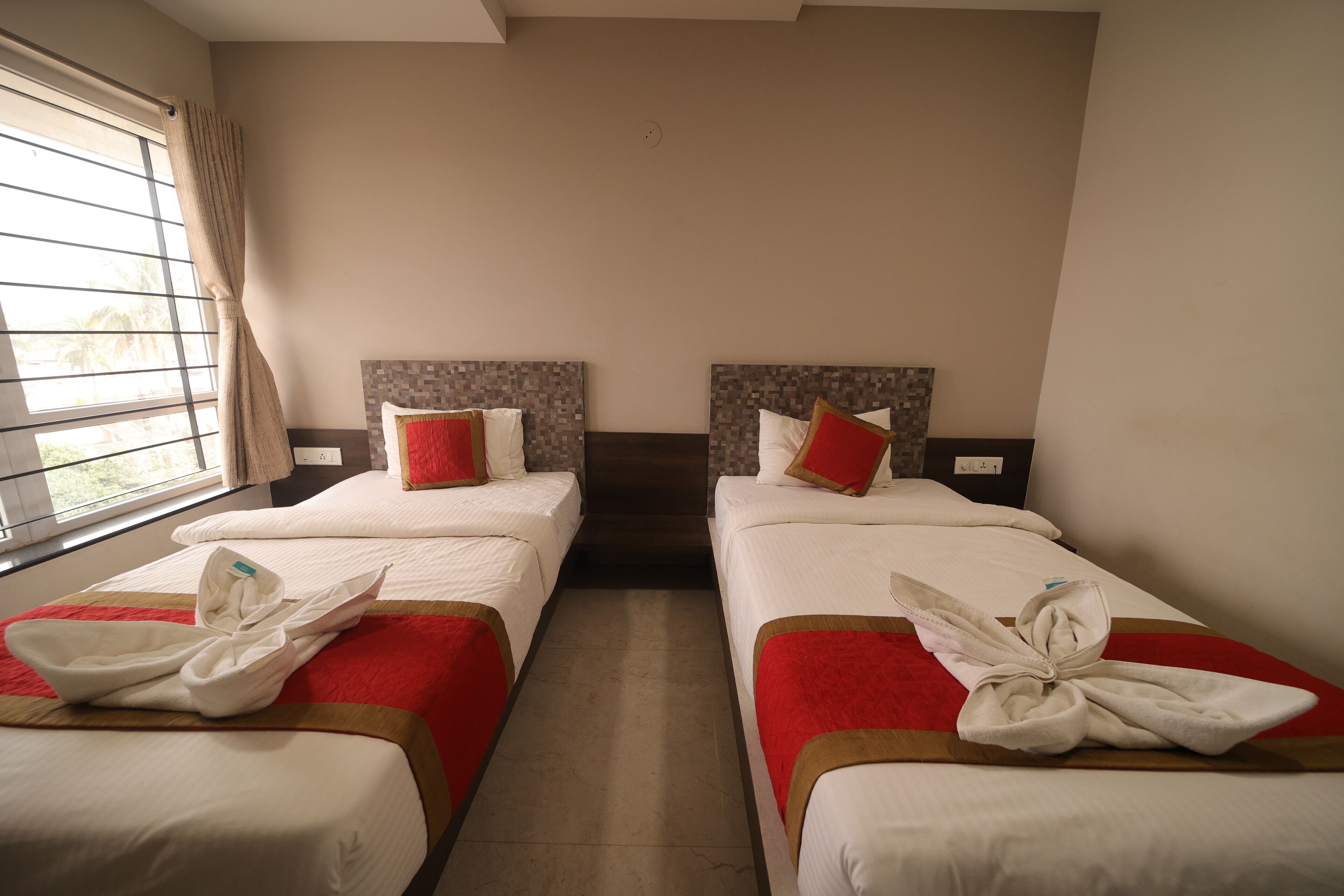 A hotel room with two beds, each with a red and white bedspread, and a window with curtains.
