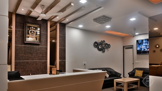 Un área de recepción moderna con un mostrador, sofás de cuero negro, una mesita de madera y un ventilador de techo.