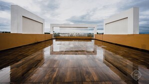 Amplia terraza moderna en la azotea con suelo húmedo que refleja el cielo y una estructura blanca al fondo.