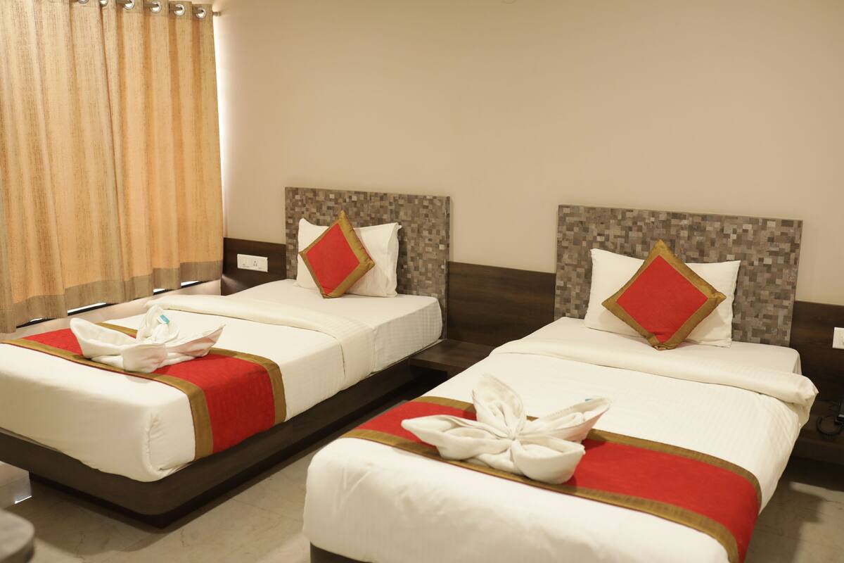 Quarto de hotel com duas camas, cada uma com colcha vermelha e dourada, almofadas brancas e travesseiro vermelho e dourado.