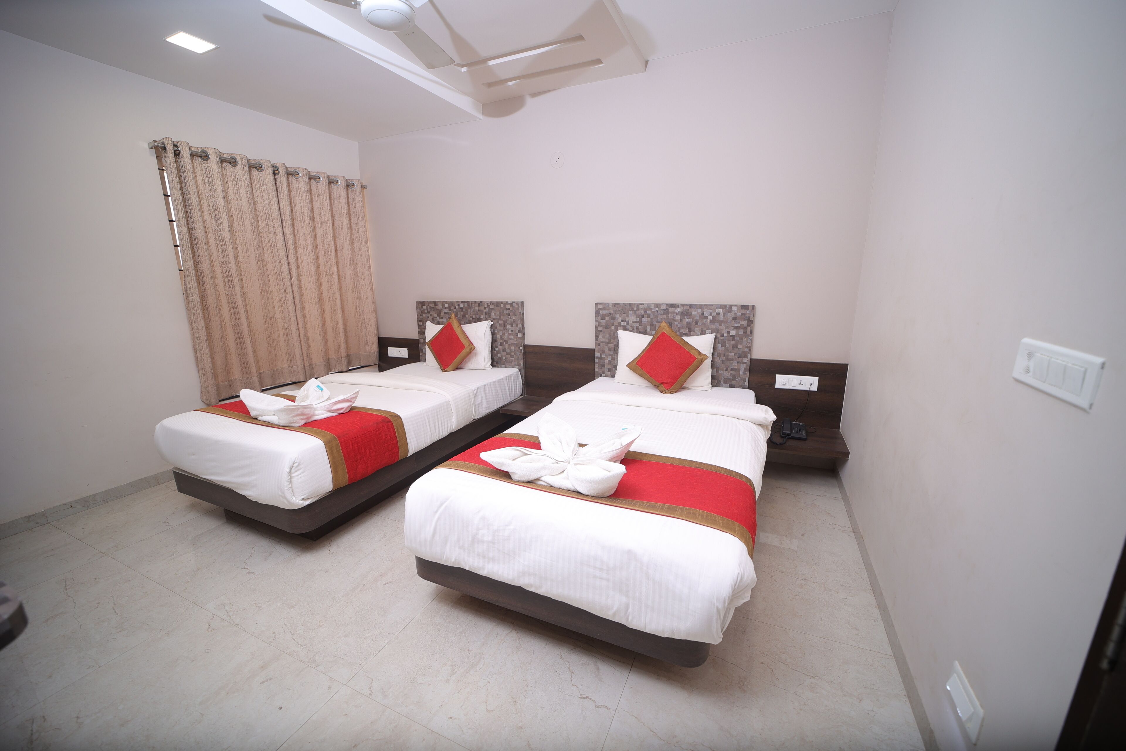 Habitación de hotel con dos camas, cada una con una colcha roja y blanca, almohadas y una toalla doblada con cuidado.