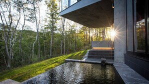 A modern building with a water feature in front, surrounded by trees. - Hanaridge Residence 11 (Kutchan)