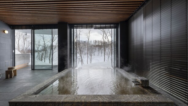 A modern indoor hot spring with a view of a snowy landscape through large windows. - Hanaridge Residence 11 (Kutchan)