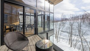 A modern room with large windows, a wicker chair, and a glass table. - Hanaridge Residence 11 (Kutchan)