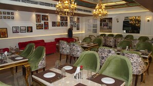 Un restaurante con sillas tapizadas de verde, mesas de mármol y obras de arte en las paredes.