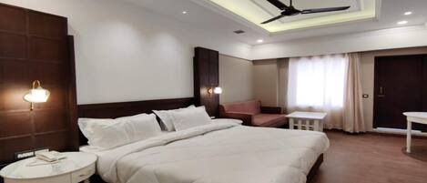A modern hotel room with a large bed, a ceiling fan, a small table, and a sofa.