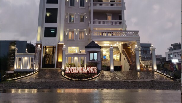 Un hotel de varios pisos con una entrada destacada, un balcón en el segundo piso y un letrero que dice "HOTEL ND MANOR".