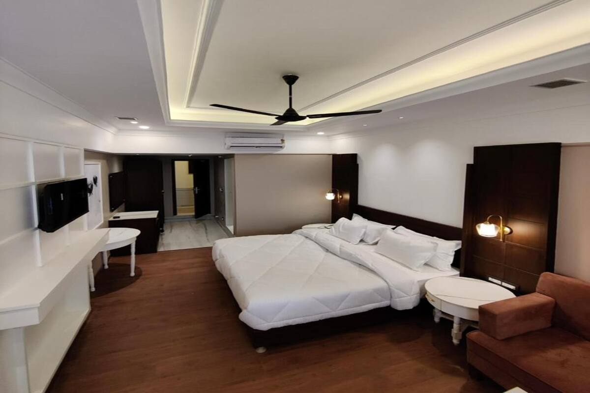 A modern hotel room with a large bed, a desk, a chair, a sofa, and a ceiling fan.