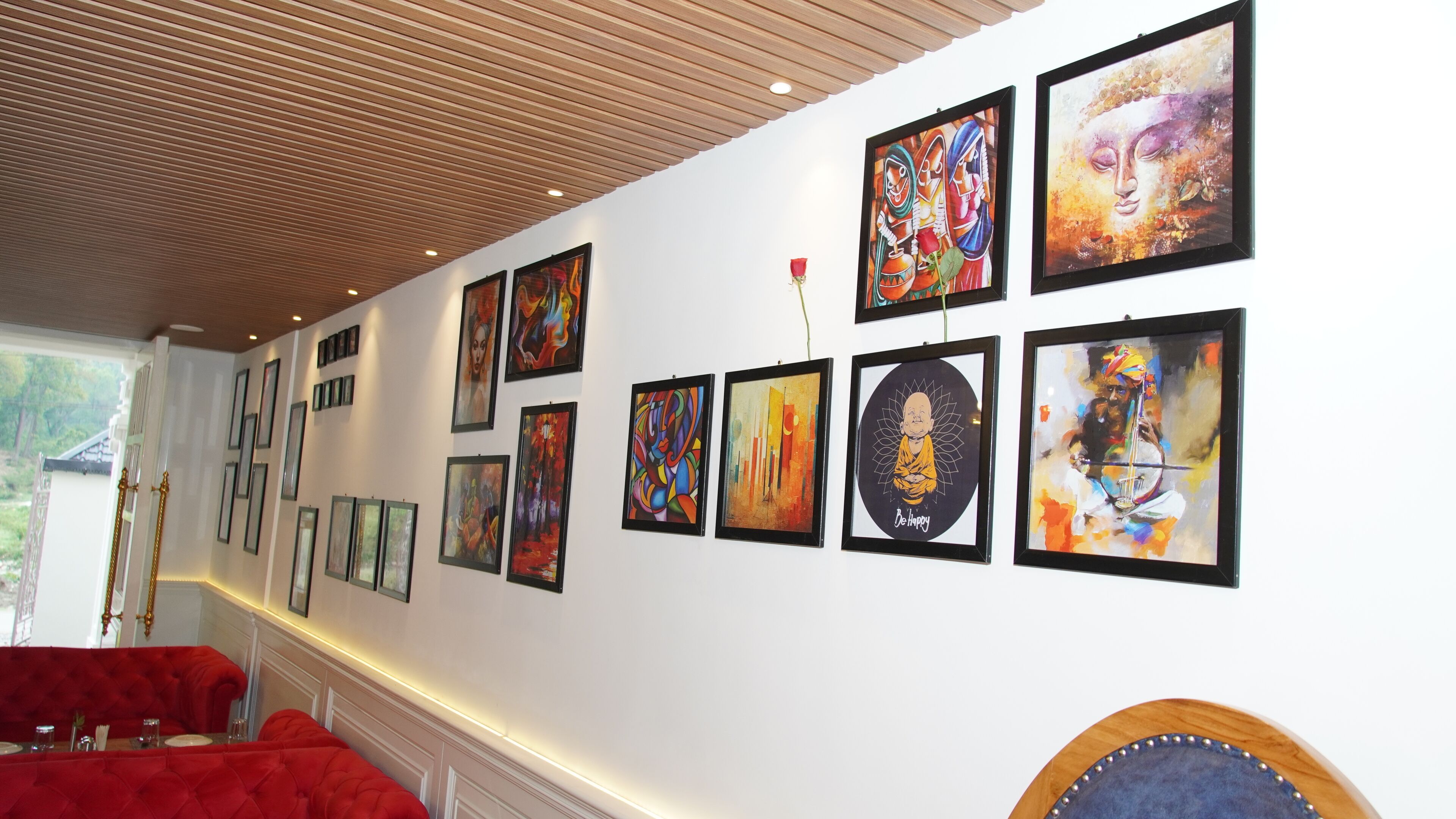 A hallway with a series of framed artworks on the wall, a red upholstered bench, and a wooden ceiling.