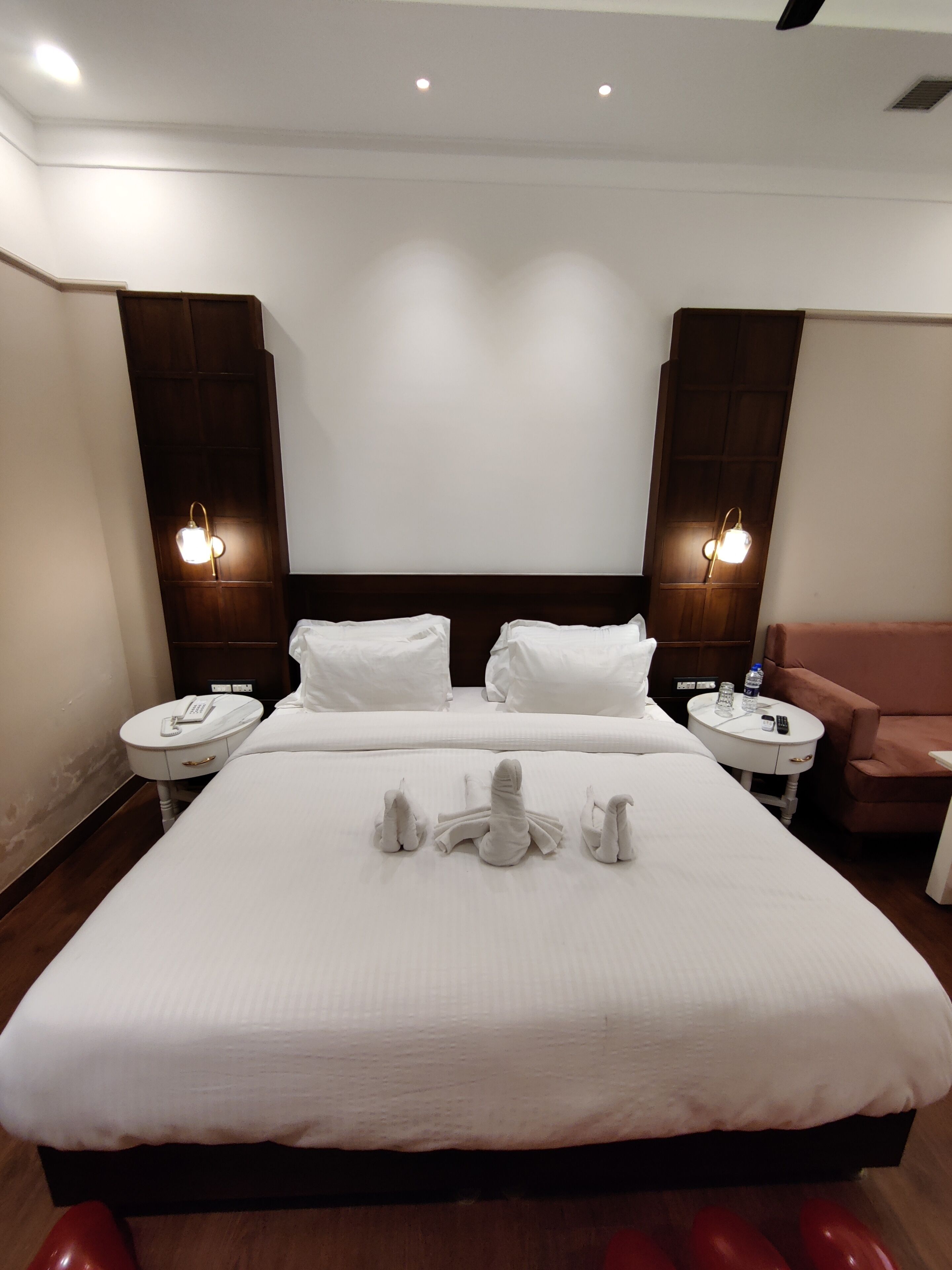 Una habitación de hotel con una cama grande, dos mesitas de noche, una lámpara de pared y una silla roja.