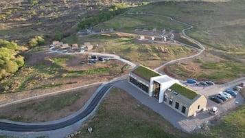 An aerial view of a modern building with a green roof, surrounded by a winding road and a series of smaller structures.