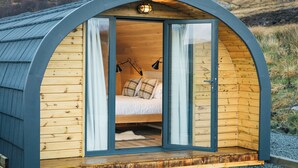 A cozy, semi-open wooden cabin with a bed, two bedside lamps, and a small window. - Bracken Hide Hotel (Portree)