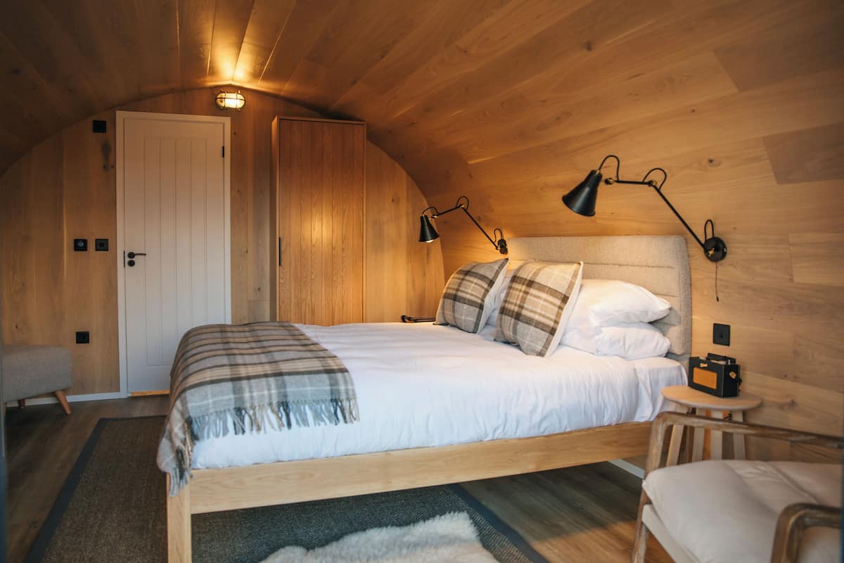 Ein gemütliches Zimmer aus Holz mit einem Bett, Nachttischlampen und einem kleinen Tisch.