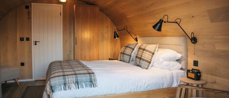 Una habitación acogedora de madera con una cama, lámparas de noche y una mesita.