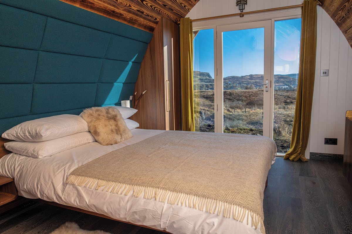 Ein Schlafzimmer mit einem großen Bett, Blick ins Freie und einer Holzbalkendecke.