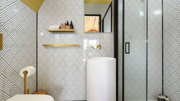 A modern bathroom with a geometric patterned wall, a large mirror, a white sink, and a glass shower enclosure.