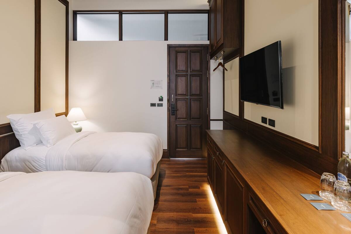 A hotel room with two beds, a wooden dresser, a TV, and a window.