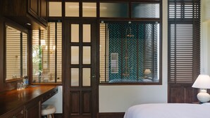 Una habitación de hotel con un escritorio de madera, una cama grande y un baño con ventana de diseño verde.