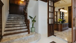 Una imponente escalera con escalones de mármol y barandillas de madera que conduce a un espacio interior bien iluminado, donde se puede ver un área de cocina a través de un umbral abierto.