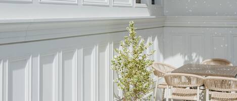 A white paneled wall with a window, a potted plant, wicker furniture, and a chandelier.