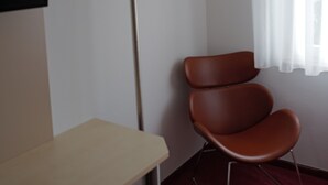Een kamer met een bureau, een stoel, een vloerlamp en een raam met dunne gordijnen.