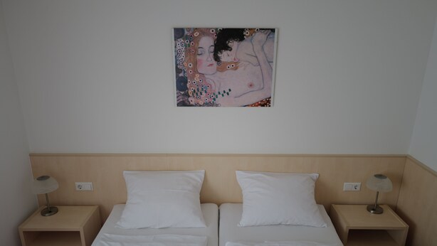 Een hotelkamer met twee bedden, witte lakens, een houten hoofdbord, nachtkastjes met lampen en een schilderij aan de muur.