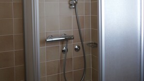 Douchecabine met een glazen deur, een handdouche en een wandmengkraan.