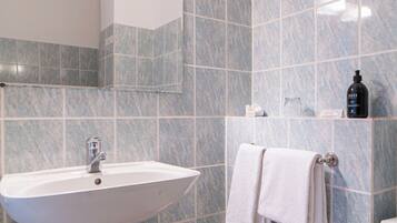 Une salle de bain comprenant un lavabo sur colonne, un miroir, un porte-serviettes, des toilettes et une poubelle.