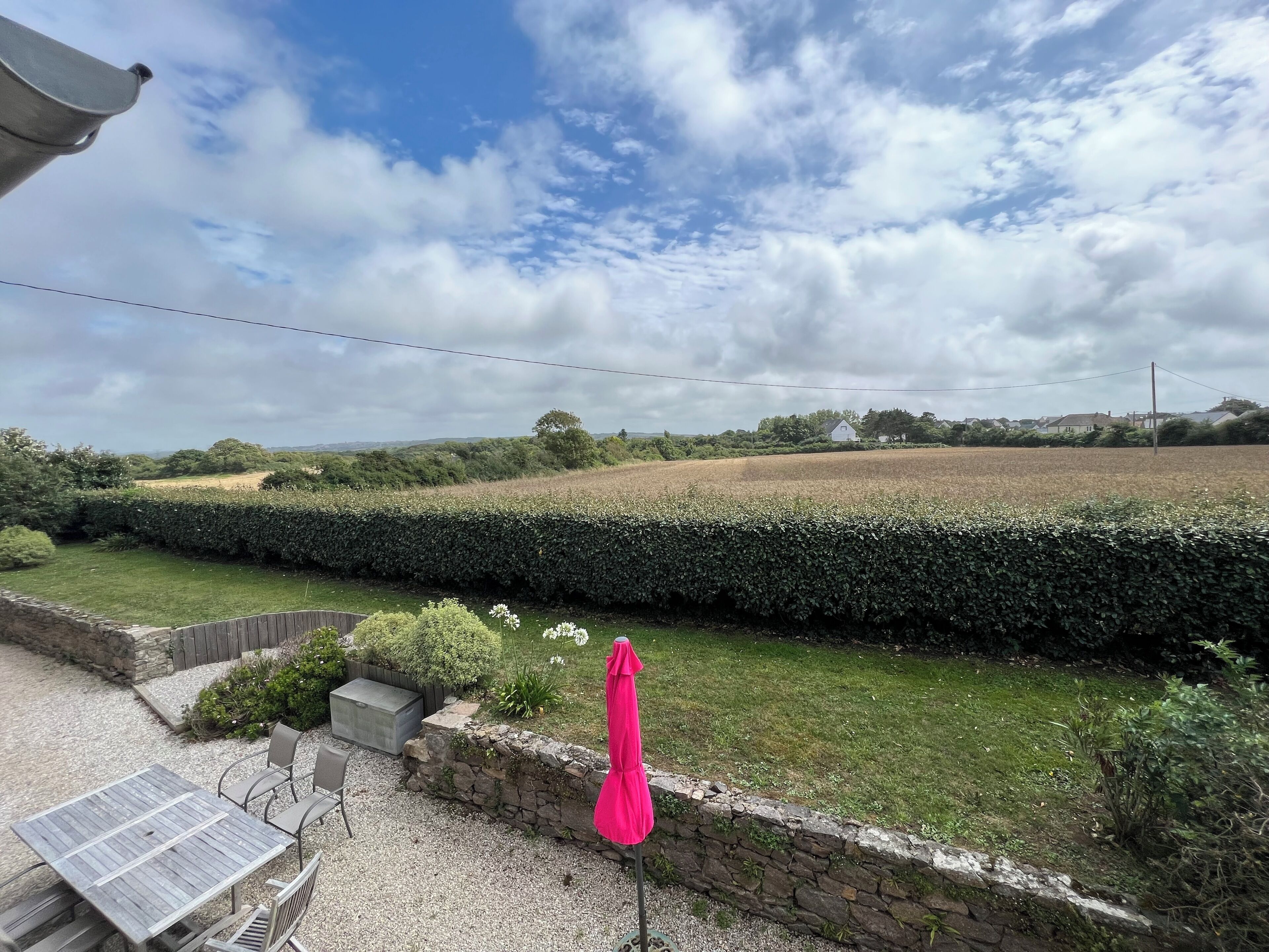 A garden with a table and chairs, a stone wall, and a field in the background.