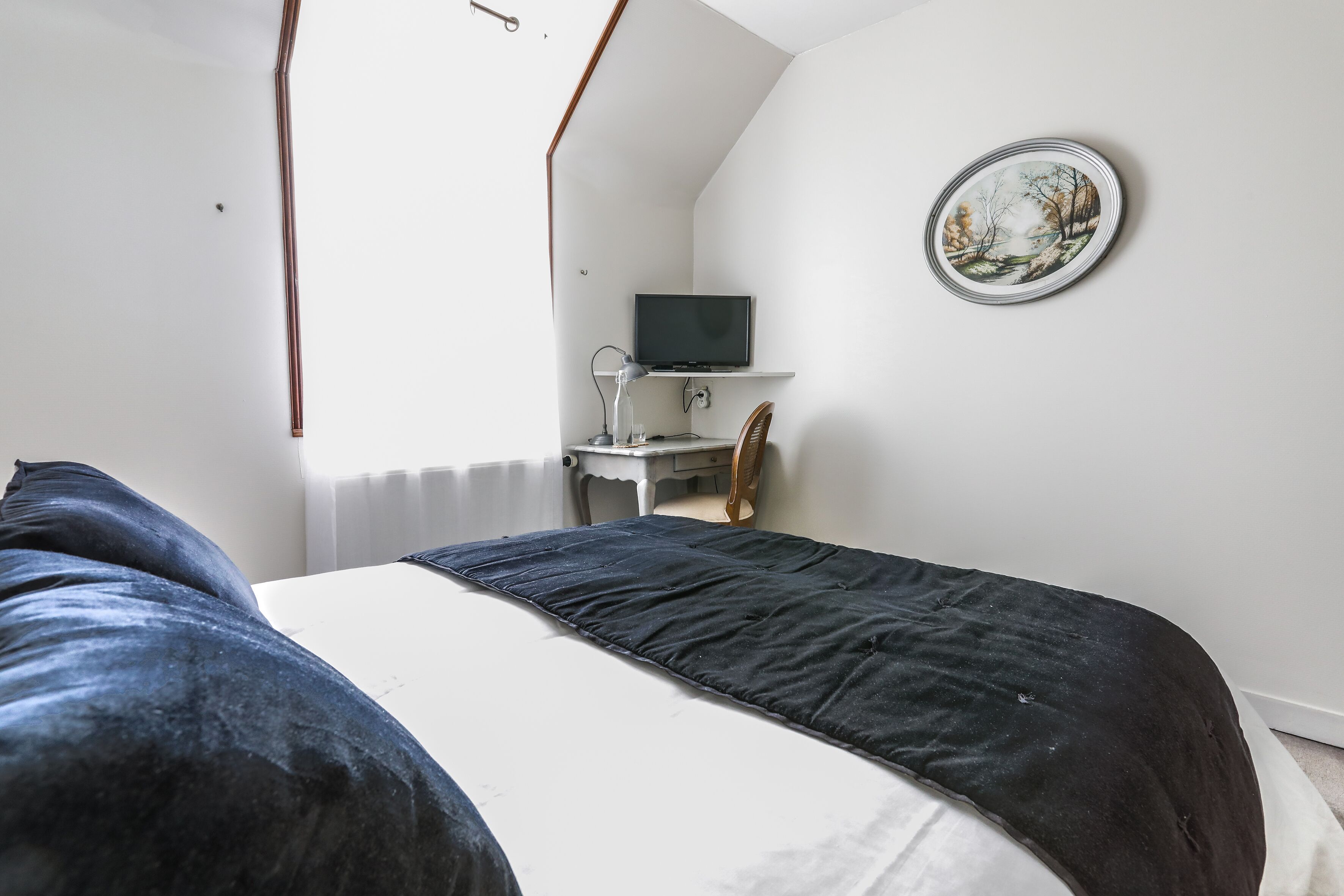 Un dormitorio con una cama, un escritorio con computadora y un televisor en un estante.