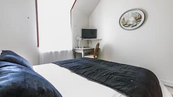 Un dormitorio con una cama, un escritorio con computadora y un televisor en un estante.