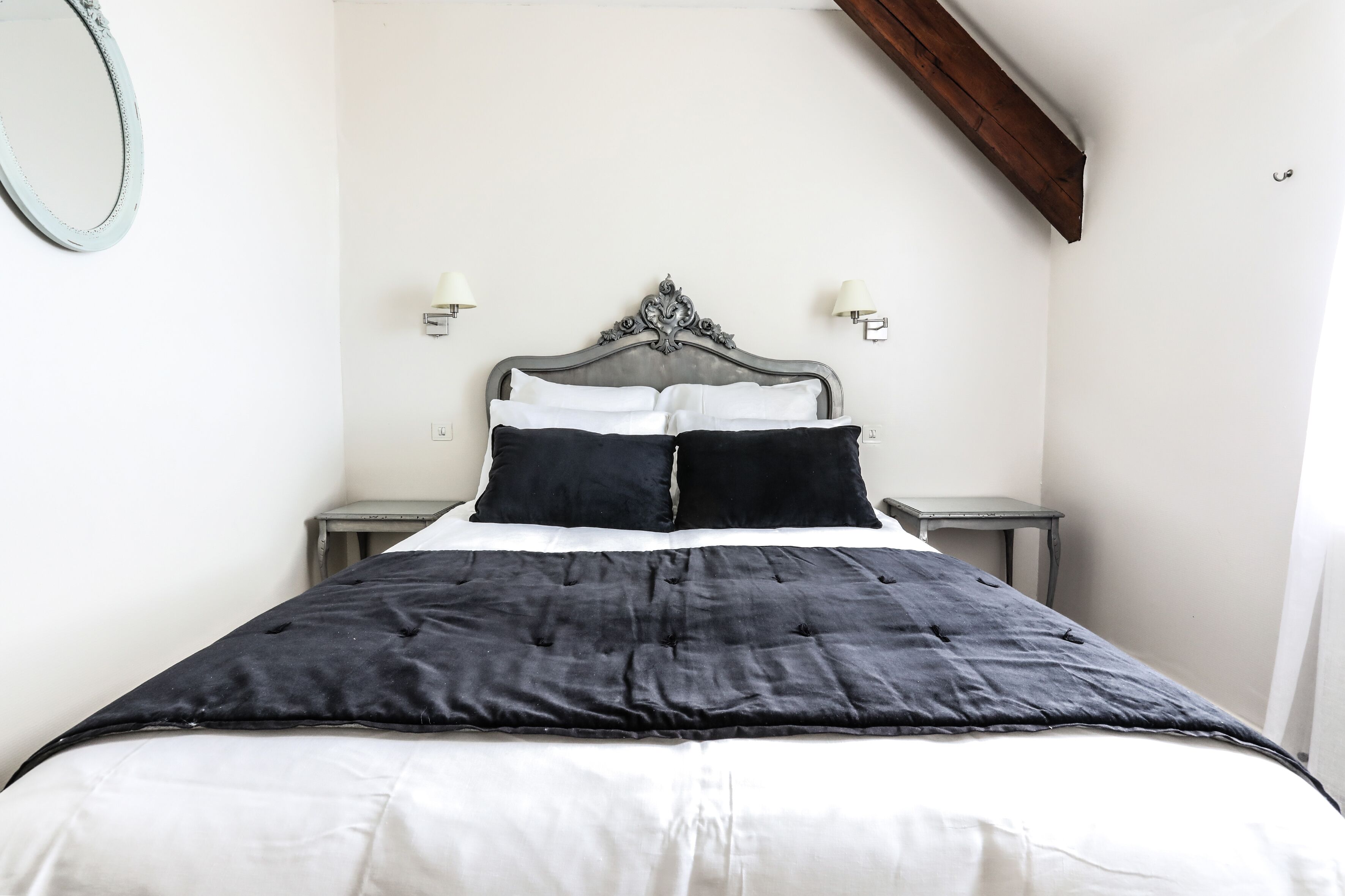 A bed with a black and white duvet, two black pillows, and a wooden headboard. There are two bedside tables with lamps on either side of the bed.