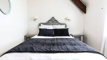 A bed with a black and white duvet, two black pillows, and a wooden headboard. There are two bedside tables with lamps on either side of the bed.