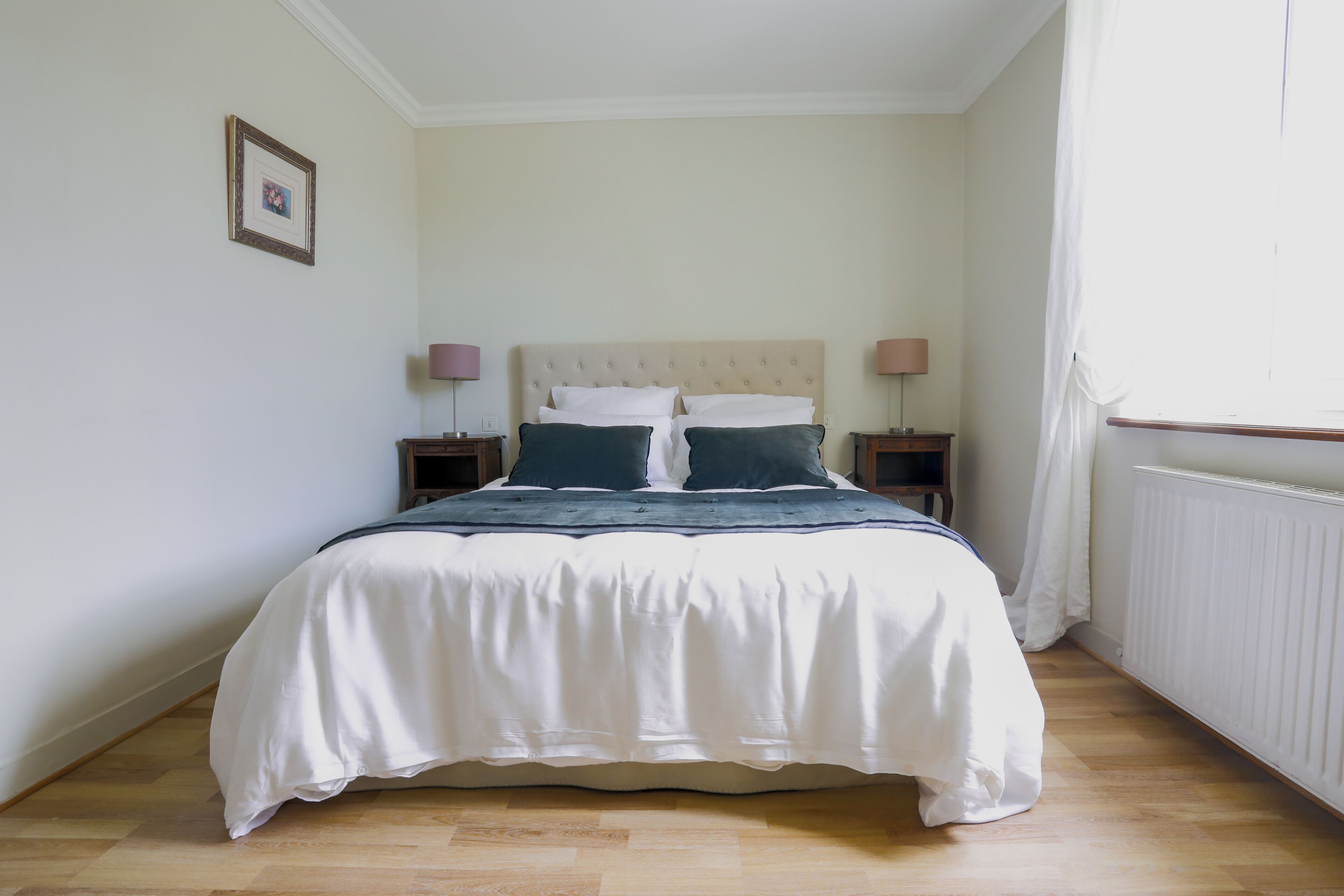 A neatly made bed with white bedding and two pillows, flanked by two bedside tables with lamps.