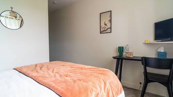 Un cuarto de hotel con una cama, un escritorio, una silla, un televisor y un cuadro en la pared.