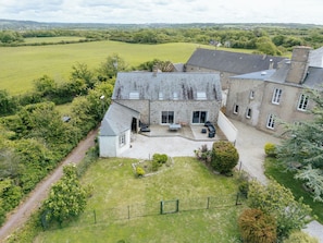 A stone house with a patio, surrounded by a fenced yard and lush greenery. - La Villa Bel Air (Flamanville)