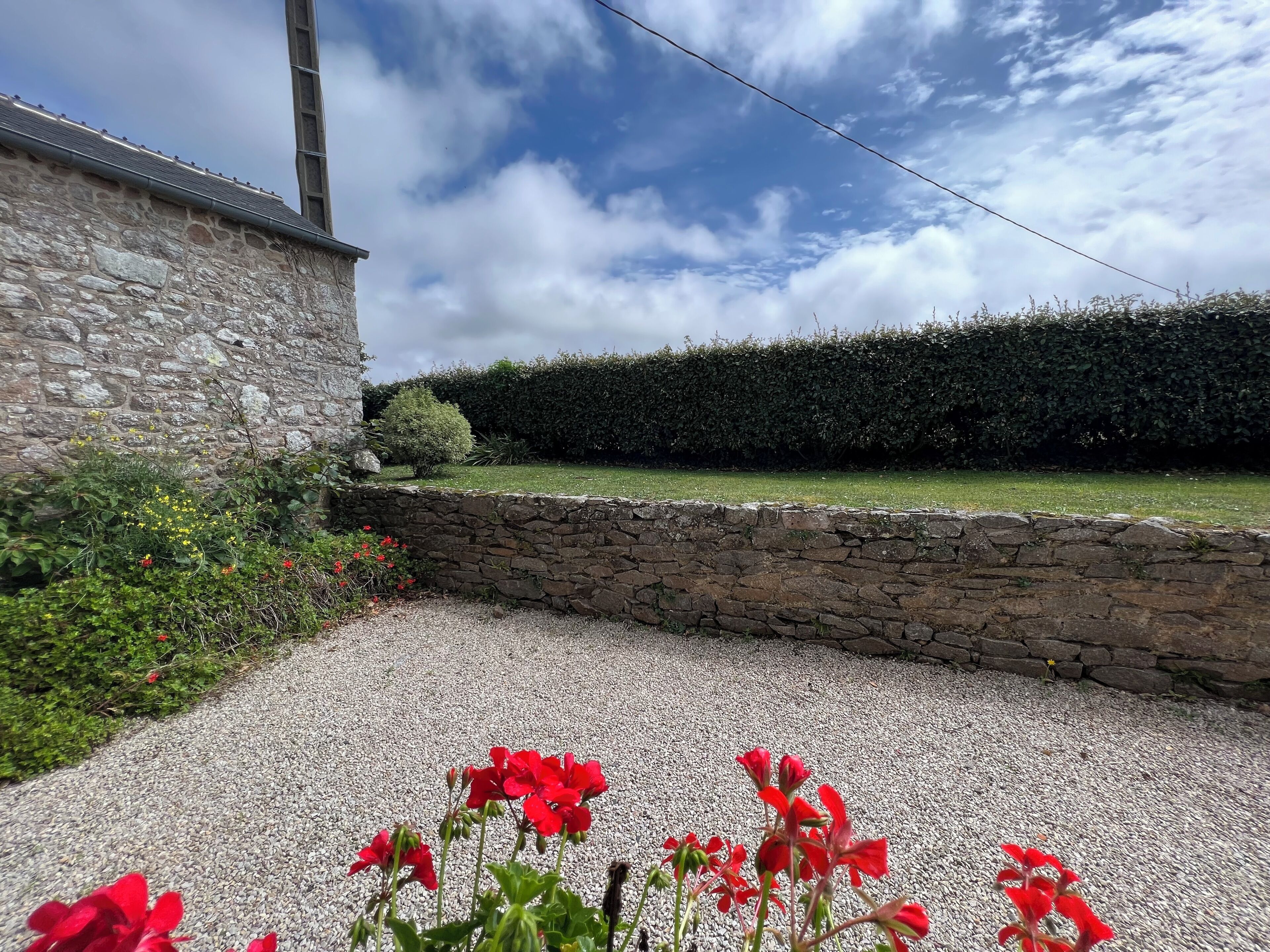 A stone building with a gravel driveway and red flowers in the foreground.