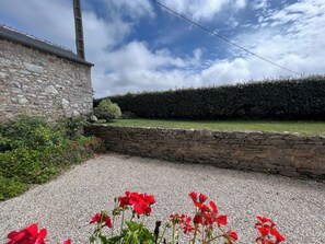 A stone building with a gravel driveway and red flowers in the foreground. - La Villa Bel Air (Flamanville)