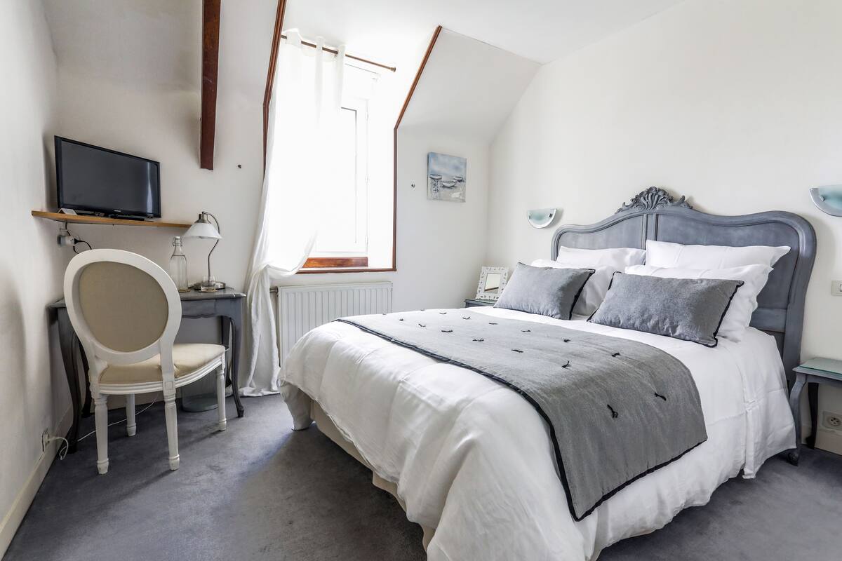 A bedroom with a bed, a chair, a desk, a television, and a window.