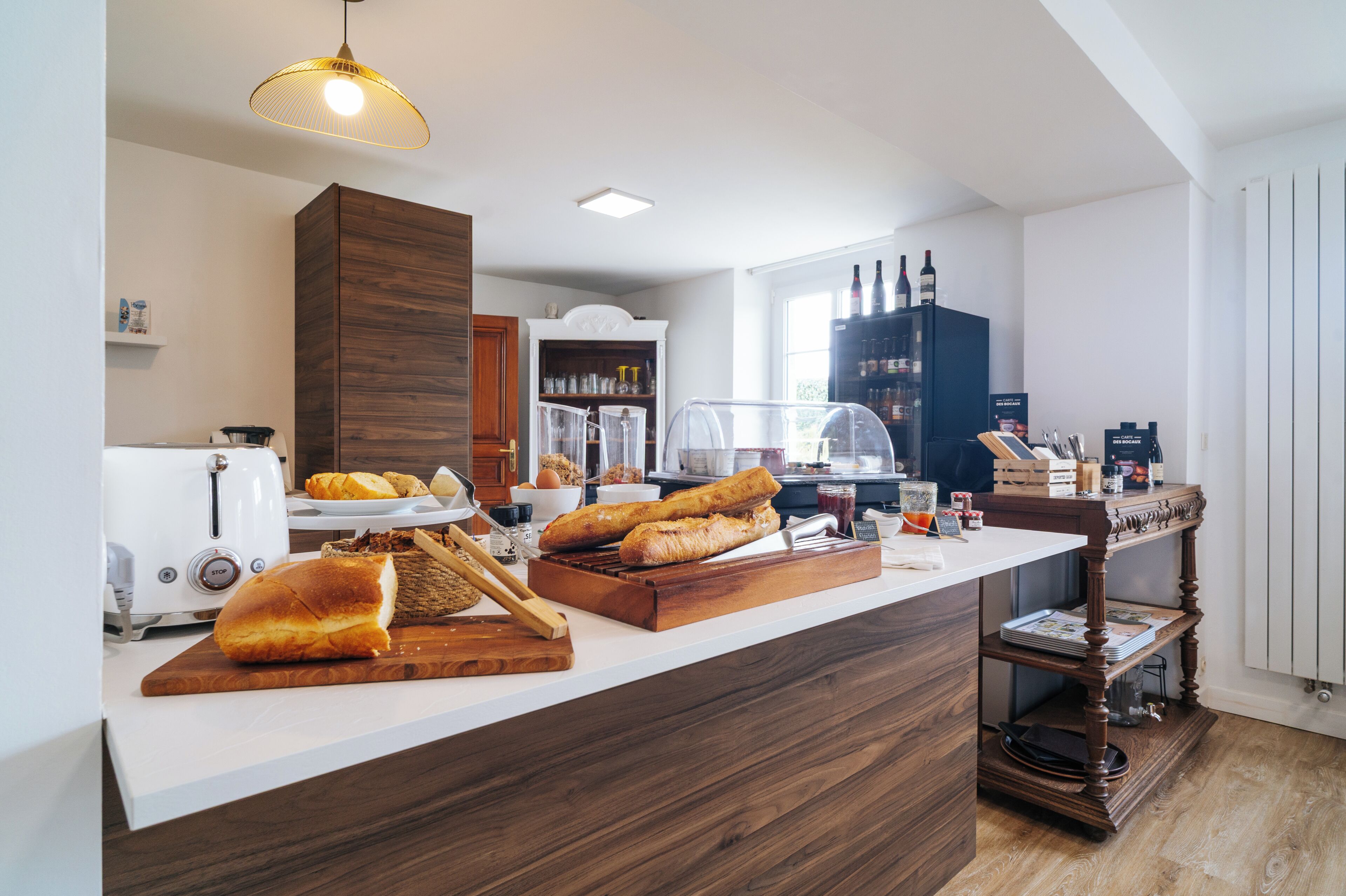 Una cocina con mostrador de madera, exhibición de pan, máquina de café y estante para vinos.