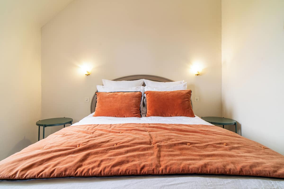 A neatly made bed with a headboard, two bedside tables, and wall-mounted lights.