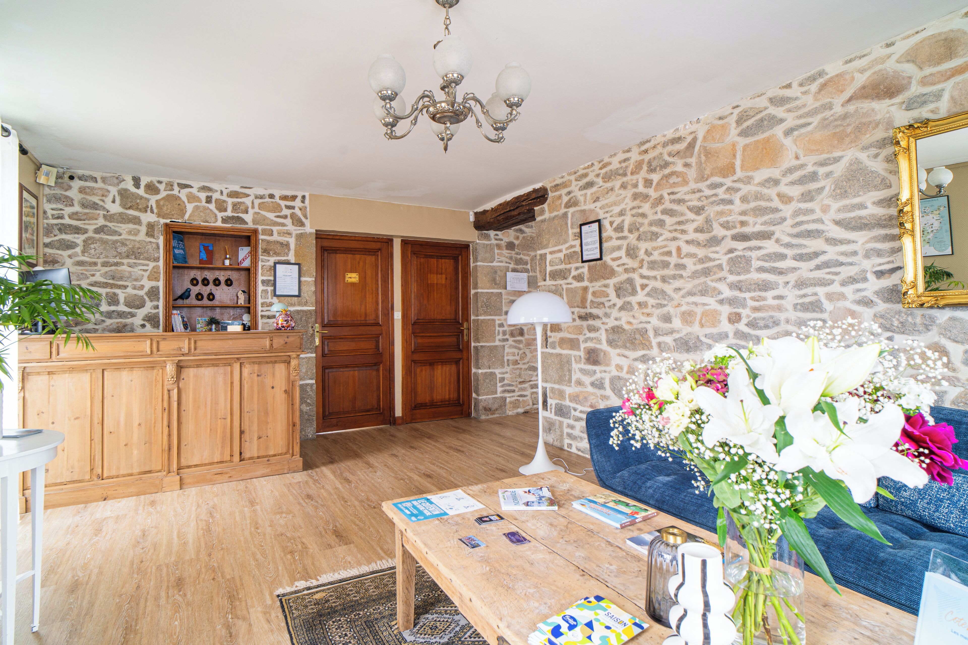 Une pièce avec un mur en pierre, des meubles en bois, un canapé bleu, une table basse avec des livres et un lampadaire.