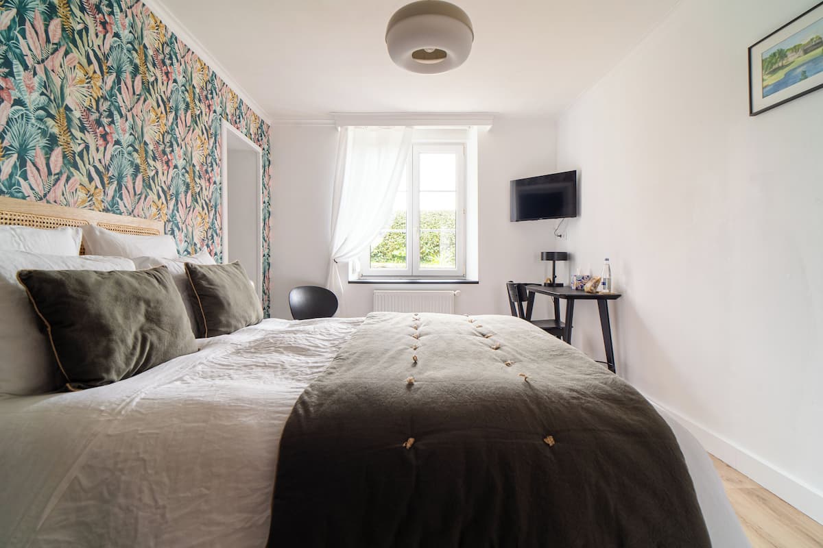 A bedroom with a bed, a chair, a desk, a television, and a window with curtains.