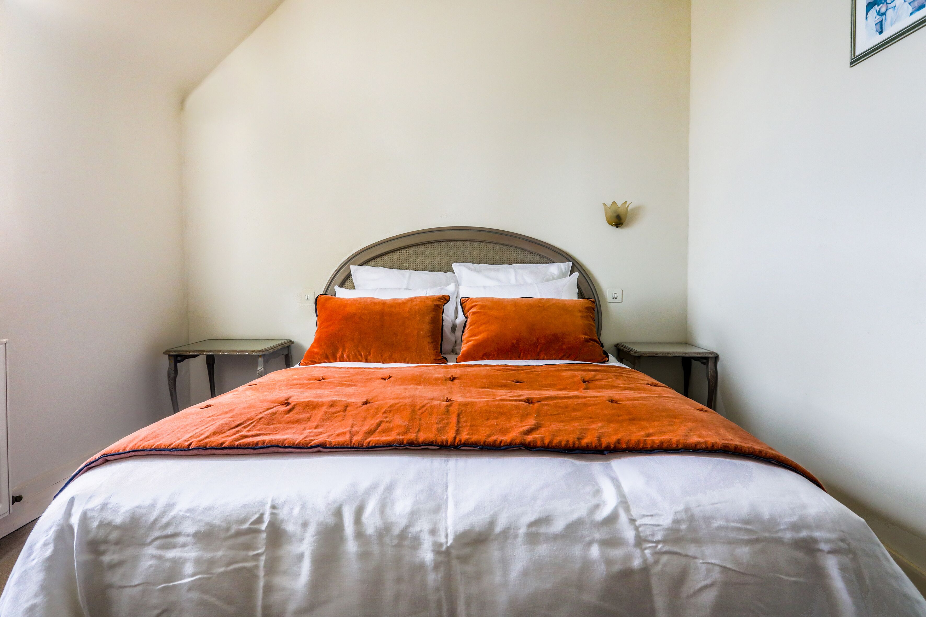 A neatly made bed with white and orange bedding, two bedside tables, and a wall-mounted light fixture.