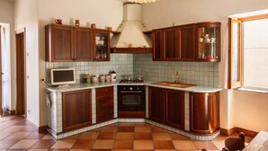 A compact kitchen with wooden cabinets, a built-in oven, a microwave, and a tiled backsplash. - House Court - Irpinia (Montemarano)