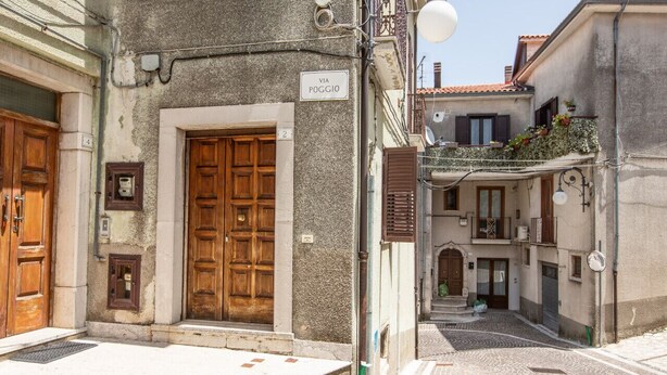 A narrow street with cobblestone pavement, a wooden door with a sign reading "VIA POGGIO", and a building with a balcony. - House Court - Irpinia (Montemarano)