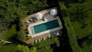 Vista aerea di una piscina rettangolare circondata da un solarium in legno, con diversi lettini e ombrelloni.
